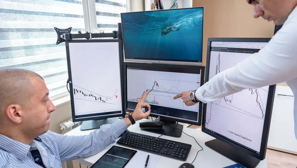 Dua orang menganalisis data di beberapa monitor, gambaran riset kompetitor SEO